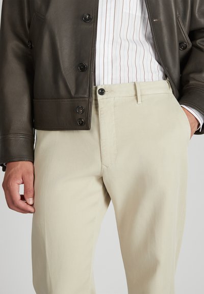 Beżowe bawełniane chinosy o gładkiej fakturze, z zamkiem błyskawicznym i zapięciem na guzik z przodu. Noszone z ciemną skórzaną kurtką i w paski koszulą.