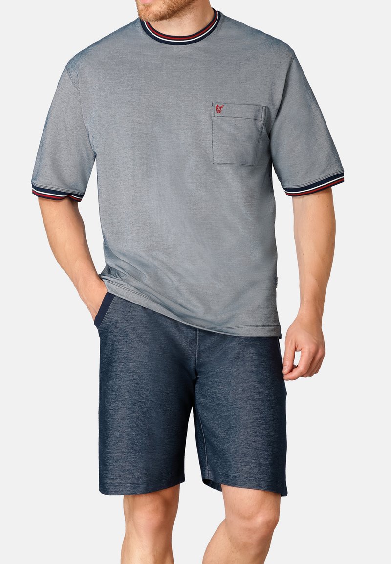 Man wearing a light blue short-sleeve shirt with a chest pocket and striped trim, paired with dark blue knee-length shorts.