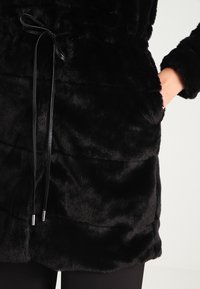 Černý kabát z umělé kožešiny se staženým pasem, s hladkým povrchem, dlouhými rukávy a předním stahovacím zavíráním.