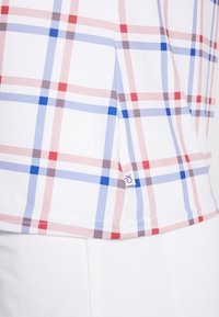 Kortärmad skjorta med vit grund och ett rutmönster i röd, blå och rosa. Inkluderar en liten logotags vid fållen.
