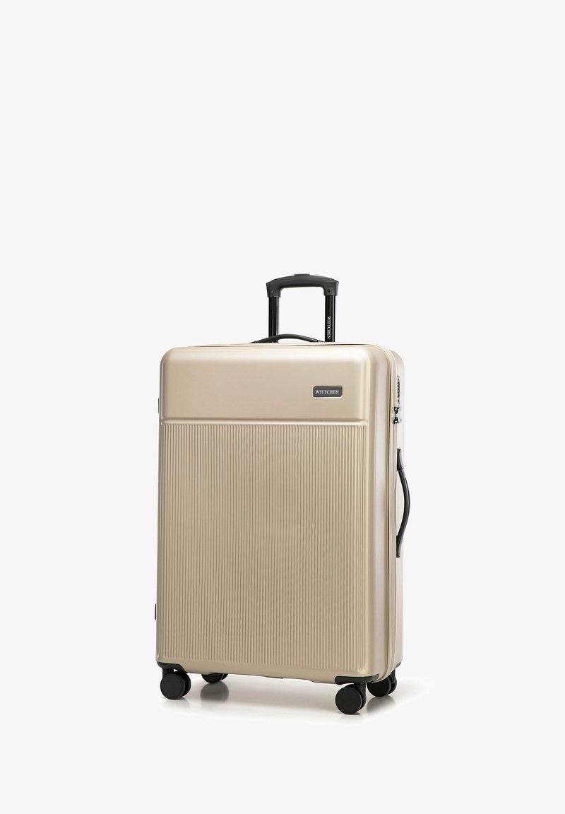 Gold hardshell suitcase with vertical ridges, a retractable handle, and four black wheels. Brand logo is on the front. Ideal for travel.