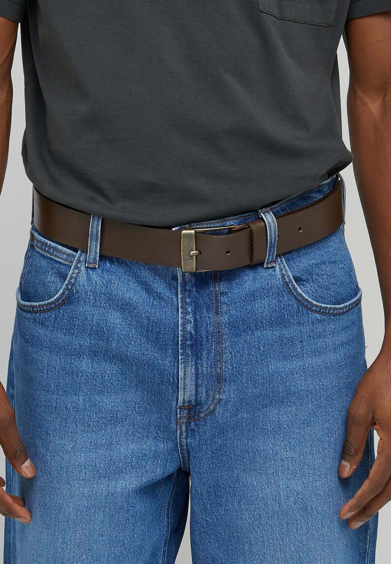 Brauner Leder-Gürtel mit einer rechteckigen Messing-Schnalle, getragen über blauen Jeans. Glatte Textur, klassisches Design und taillierte Passform.