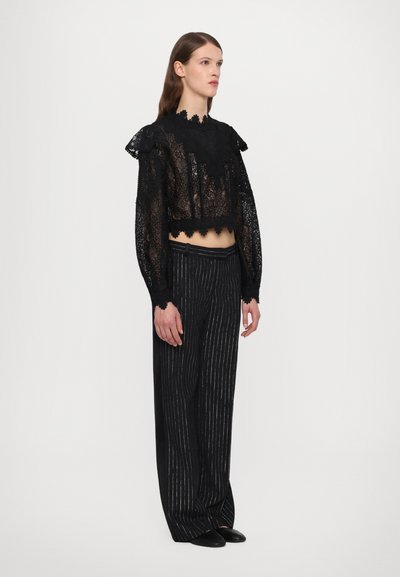Black lace crop top with ruffled edges, paired with black and silver pinstriped wide-leg trousers. Smooth texture, loose fit.