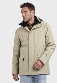 Beige wasserfeste Jacke mit einem Reißverschluss an der Vorderseite, verstellbarer Kapuze und zwei seitlichen Taschen. Besondere Merkmale sind die strukturierte Oberfläche und der kontrastierende schwarze Kragen.