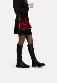 Black knee-high boots with a textured finish and chunky soles, paired with a shiny burgundy handbag, worn with a black dress.