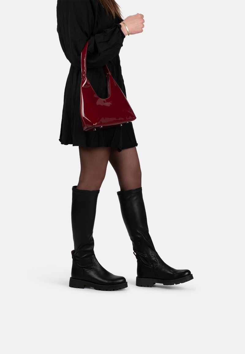 Black knee-high boots with a textured finish and chunky soles, paired with a shiny burgundy handbag, worn with a black dress.