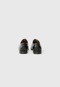 Zapatos de cuero negro con un acabado suave, punteras redondeadas y tacón bajo. Textura sutil en los laterales, forro interior en marrón.