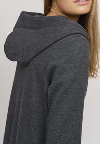 Grå hettegenser med teksturert stoff, med en fremtredende hette og en avslappet passform. Myk, uformell stil, perfekt for lagdeling.