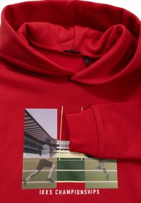 Sudadera roja con capucha doblada y un estampado gráfico de un jugador en movimiento. El material es suave y cuenta con detalles de puños acanalados.