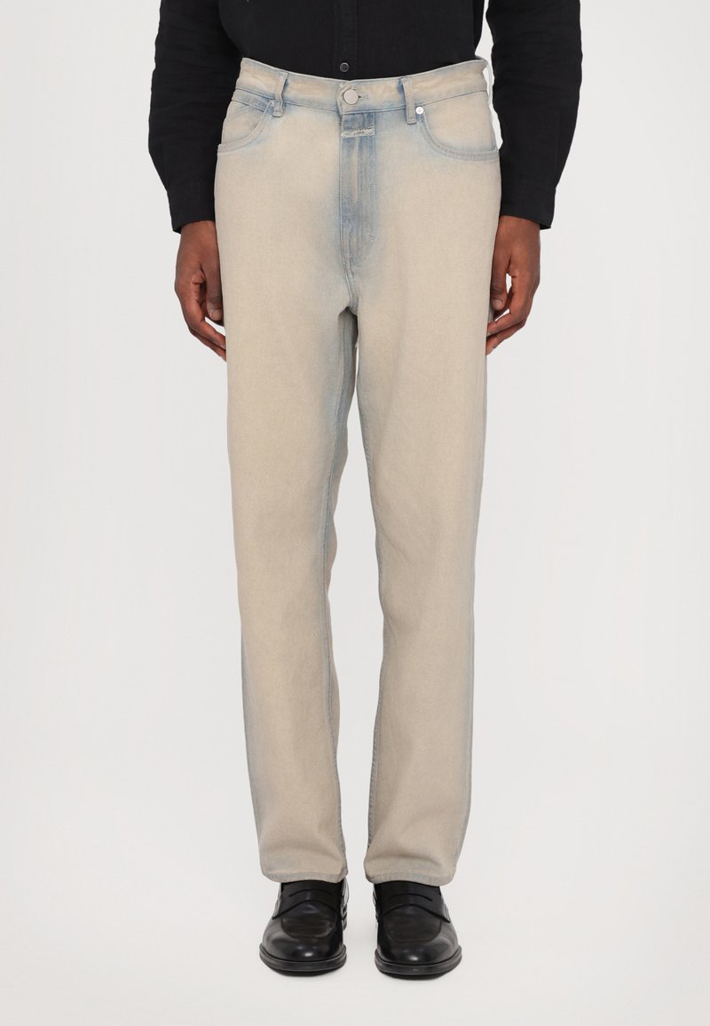 Pantaloni in denim azzurro chiaro con un aspetto leggermente sbiadito, design a gamba dritta, cinque tasche e chiusura a bottone argentato, indossati con scarpe nere.