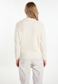Maglione crema a costine con colletto a risvolto e maniche lunghe, abbinato a pantaloni grigi chiari, visto da dietro.