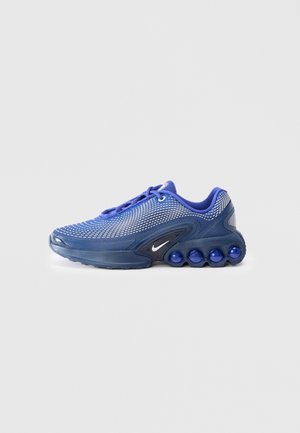 Chaussure de sport bleue avec dessus en mesh, lacets et sphères de rembourrage visibles dans la semelle, montrée de côté sur un fond clair.