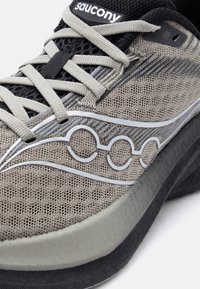 Γκρι και μαύρο αθλητικό παπούτσι Saucony με επάνω μέρος από δίχτυ, ανοιχτό γκρι κορδόνια και χαρακτηριστικό λογότυπο Saucony στο πλάι κοντά στη σόλα.