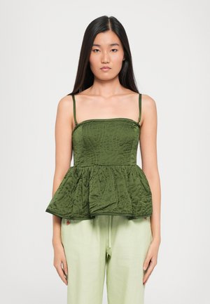 Green quilted peplum top with thin straps, featuring textured stitching and a flared design. Paired with light green trousers.