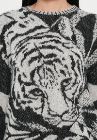 Strickpullover mit einem schwarz-weißen Tigerdesign, Rundhalsausschnitt und verschiedenen Texturen, einschließlich weicher und flauschiger Fasern.