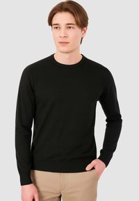 Maglione nero a maniche lunghe realizzato in un tessuto a maglia liscia. Presenta un colletto rotondo, polsini a coste e vita aderente.