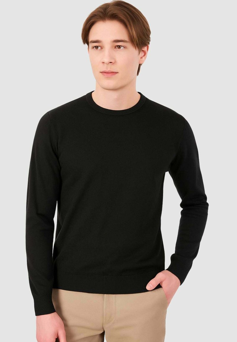 Maglione nero a maniche lunghe realizzato in un tessuto a maglia liscia. Presenta un colletto rotondo, polsini a coste e vita aderente.