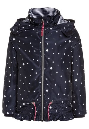 Granatowa dziecięca kurtka przeciwdeszczowa w białe kropki, z wewnętrznym kołnierzem w paski, przednim zamkiem błyskawicznym, sznurkami z czerwonymi końcówkami i falbanami na dole.