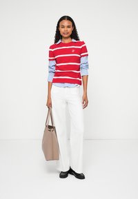 Red and white striped sweater with a blue collared shirt underneath, paired with white pants and a beige tote bag. Black shoes.