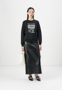 Svart hettegenser med hvitt grafikk, parret med en høy midje svart skinnskjørt, hvit kviltet håndveske og svarte stilettos.