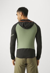 Men's hoodie with a black body and olive green panels, featuring a hood with a contrasting red line. Made from smooth, lightweight fabric.