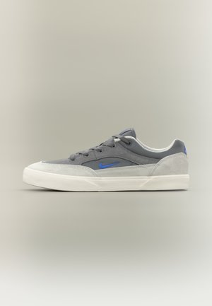 Sneaker grigia con una combinazione di materiali in camoscio e lisci, logo con accento blu, punta arrotondata, suola in gomma bianca e design classico con lacci.