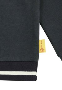 Sudadera gris oscuro con puños acanalados. Presenta una etiqueta de marca amarilla y un acento a rayas en negro y blanco en el dobladillo inferior.