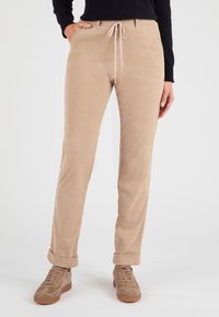 Beige corduroy broeken met een relaxte pasvorm, een elastische tailleband, een verstelbaar trekkoord en omgeslagen pijpen. Gepaard met beige sneakers.