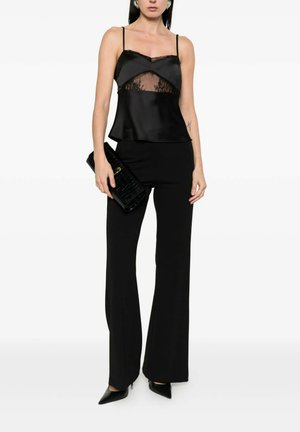 Donna che indossa un top nero senza maniche con rifiniture in pizzo, pantaloni neri a vita alta, tacchi neri appuntiti e tiene in mano una pochette nera con texture.