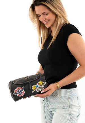 Sac en tissu gris avec fermeture éclair, orné de patchs colorés, y compris un œil bleu avec des ailes et un patch logo. Forme compacte et rectangulaire.