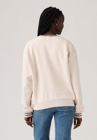 Pullover sweatshirt in lichtbeige, zachte stof, oversized pasvorm, met gestreepte zwart-wit accenten op de manchetten en halslijn.