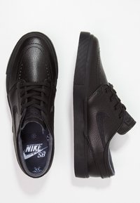 Svarta Nike SB-sneakers har en texturerad läderöverdel, rund tå, snörning och en platt gummisula med fiskbensmönster.