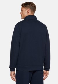 Felpa blu navy con colletto alto, tessuto textures e polsini a costine. Presenta un orlo dritto e un branding discreto sulla manica.