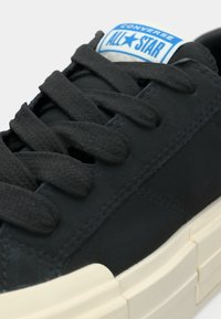 Sneaker nera in tela con punta arrotondata, suola spessa color crema e lacci piatti. Etichetta blu e bianca sulla linguetta con la scritta "Converse All Star".