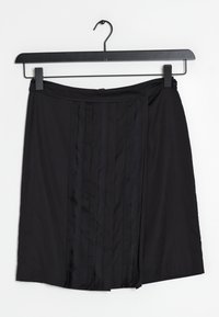 Černá sukně vyrobená z hladkého materiálu, se svislými sklady a plochým pasem. Visí na černém ramínku na bílém pozadí.