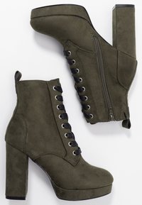 Bottines en suède vert olive avec des talons en bloc hauts, à lacets à l'avant et zip sur le côté. Caractéristiques de lacets noirs et d'œillets en métal.