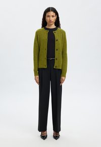 Žalias megztas kardiganas su apvalia iškirpte, sagomis užsegamas ir ilgomis rankovėmis, derinamas su juodomis plačiomis kelnėmis ir juodais smailiais aukštakulniais.