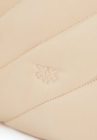 Μπεζ κεντημένο ύφασμα με διαγώνια ραφή και κεντημένο λογότυπο φύλλου. Μαλακή υφή, διακριτική γυαλάδα, μινιμαλιστικός σχεδιασμός.