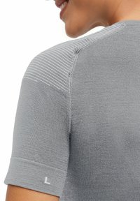 Szara koszula z krótkim rękawem o fakturowanym wykończeniu, z prążkowanym wzorem na ramieniu oraz małą białą etykietą z literą "L" na rękawie.