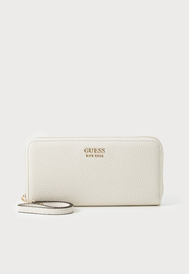 Portefeuille en cuir blanc avec une surface texturée, des accessoires en métal doré et une sangle pour le poignet. Le nom de la marque "GUESS" est embossé à l'avant.