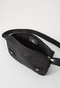 Borsa a tracolla nera in nylon con scomparto principale con zip, tracolla regolabile e dettagli in metallo argentato. L'interno è privo di motivi.