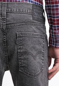 Šedé džíny z denimu s úzkým střihem, s zadní kapsou se charakteristickým vyšitým obloukovým vzorem a koženou značkovou nášivkou na pasu.