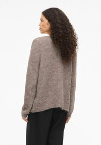 Brūns adīts džemperis ar brīvu piegriezumu, garām piedurknēm un nedaudz garāku aizmugures apmalīti. Mīksta faktūra un minimālistisks dizains.