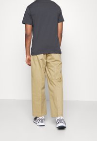 T-shirt gris à manches courtes, pantalons beiges amples et baskets gris et noires. Design simple, matériau respirant et couleurs neutres.