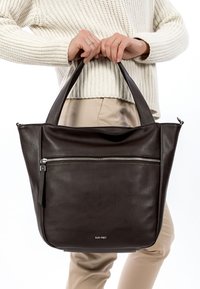 Bruine leren handtas met dubbele handgrepen, voorzien van een voorvak met rits en een gladde textuur. Merkennaam onderaan weergegeven.