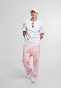 White short-sleeve t-shirt, light pink sweatpants, and matching cap. Includes sunglasses on shirt. White sneakers complete the outfit.