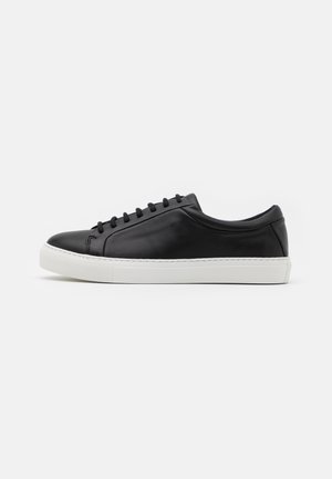 Czarny, skórzany niski sneaker z czarnymi sznurowadłami i grubą, białą gumową podeszwą na jednolitym białym tle.