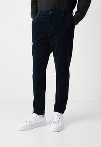 Námořnické kordové kalhoty slim fit s bočnými kapsami a jedním knoflíkem, doplněné bílými teniskami. Hladká textura a vertikální žebrování.