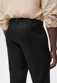Black linen trousers with a smooth texture, featuring a rear pocket with a button closure and a waistband. The fabric has a subtle sheen.