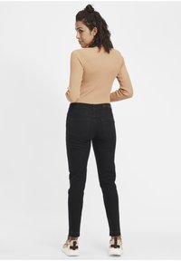 Jean noir à coupe slim, taille mi-haute, avec poches arrière, associé à un haut beige côtelé. Les chaussures comprennent des baskets beiges et brunes.